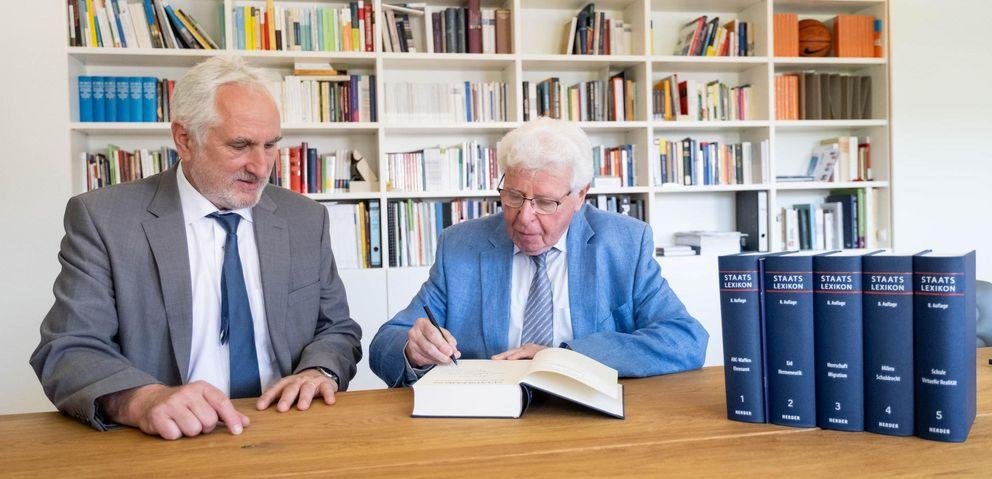 Der Präsident der Universität Passau Professor Dr. Ulrich Bartosch sitzt mit Professor Oberreuter vor einem Bücherregal. Vor ihnen sind die Bänder des Staatslexikons aufgestellt 